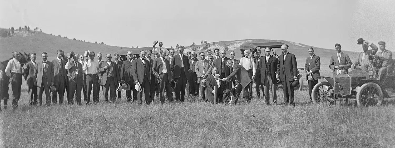 Group of people lined up watching a person hammer a stake in the ground